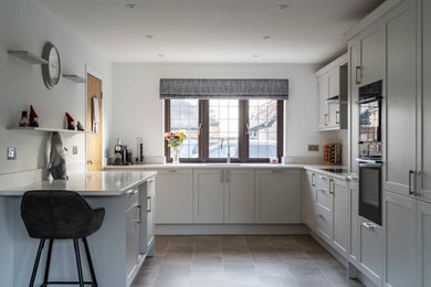 Design ideas for a medium sized traditional enclosed kitchen in Oxfordshire with a single-bowl sink, recessed-panel cabinets, grey cabinets, quartz worktops, black appliances, grey floors and white worktops.