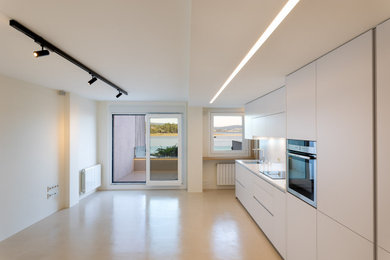 Modelo de cocina lineal y beige y blanca contemporánea de tamaño medio abierta con fregadero bajoencimera, armarios con paneles lisos, encimera de cuarzo compacto, salpicadero blanco, puertas de cuarzo sintético, electrodomésticos de acero inoxidable, suelo beige, encimeras blancas y microcemento