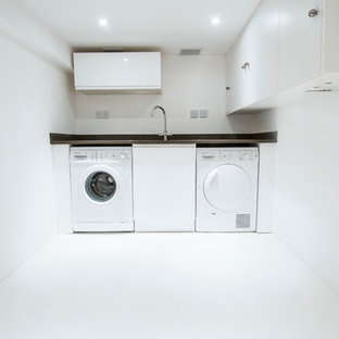 Photo of a medium sized modern single-wall separated utility room in London with a submerged sink, flat-panel cabinets, white cabinets, granite worktops, white walls, concrete flooring and a side by side washer and dryer.
