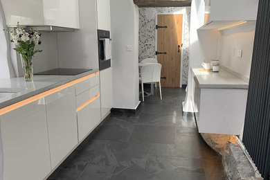 This is an example of a medium sized contemporary galley kitchen/diner in Other with a single-bowl sink, flat-panel cabinets, white cabinets, concrete worktops, grey splashback, cement tile splashback, black appliances, slate flooring, no island, black floors, grey worktops and exposed beams.