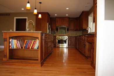 Example of a classic kitchen design in Other with raised-panel cabinets, medium tone wood cabinets, granite countertops, beige backsplash, ceramic backsplash, stainless steel appliances and an island