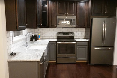 Example of a classic l-shaped dark wood floor kitchen design in New York with a farmhouse sink, recessed-panel cabinets, dark wood cabinets, quartzite countertops, white backsplash, subway tile backsplash and stainless steel appliances