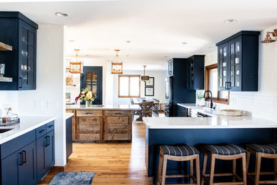 Inspiration for a large transitional u-shaped medium tone wood floor and brown floor open concept kitchen remodel in Phoenix with a farmhouse sink, shaker cabinets, blue cabinets, quartz countertops, white backsplash, subway tile backsplash, black appliances, two islands and gray countertops