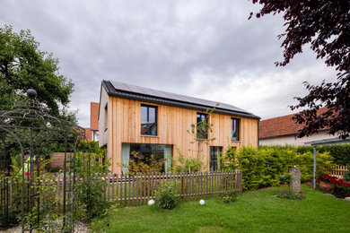 This is an example of a contemporary two-storey beige house exterior in Munich with wood siding, a gable roof, a tile roof, a grey roof and clapboard siding.