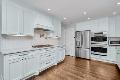 Large minimalist medium tone wood floor and brown floor eat-in kitchen photo in Other with recessed-panel cabinets, white cabinets, quartzite countertops, white backsplash, subway tile backsplash, stainless steel appliances, no island, white countertops and a drop-in sink