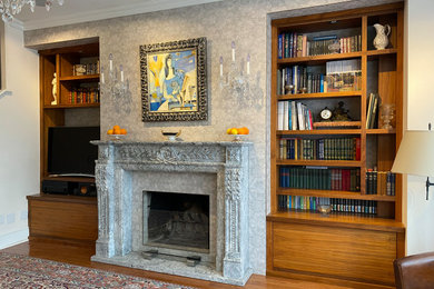 Diseño de biblioteca en casa abierta moderna de tamaño medio con paredes grises, suelo de madera en tonos medios, marco de chimenea de piedra, televisor independiente y suelo marrón