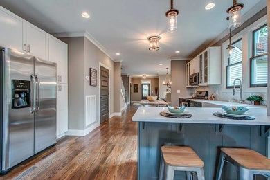Mid-sized transitional u-shaped medium tone wood floor and brown floor open concept kitchen photo in Nashville with an undermount sink, shaker cabinets, gray cabinets, quartz countertops, white backsplash, marble backsplash, stainless steel appliances and an island
