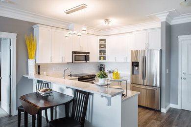 Mid-sized contemporary u-shaped eat-in kitchen in Vancouver with white cabinets, white splashback, no island, brown floor, shaker cabinets and quartz benchtops.