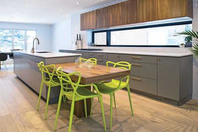 Large minimalist galley light wood floor eat-in kitchen photo in Toronto with flat-panel cabinets, gray cabinets, white backsplash, white countertops, an undermount sink, black appliances and an island