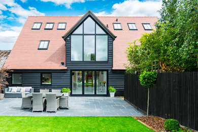 Inspiration for a large contemporary two-storey black house exterior in Hertfordshire with wood siding, a gable roof and a tile roof.