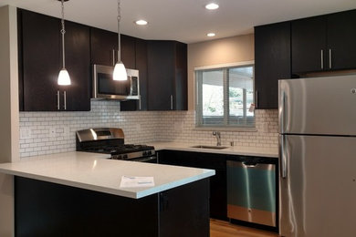 Inspiration for a small u-shaped medium tone wood floor open concept kitchen remodel in San Francisco with an undermount sink, flat-panel cabinets, dark wood cabinets, quartz countertops, white backsplash, ceramic backsplash, stainless steel appliances and a peninsula