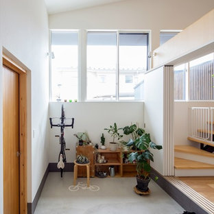 他の地域の大きい片開きドアコンテンポラリースタイルのおしゃれな玄関ラウンジ (白い壁、コンクリートの床、淡色木目調のドア、グレーの床) の写真