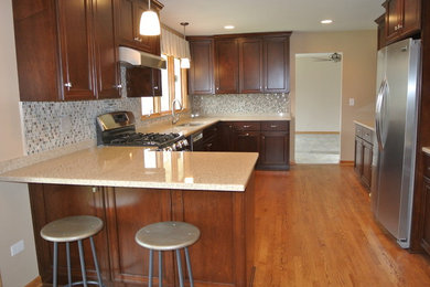 1960s u-shaped medium tone wood floor open concept kitchen photo in Chicago with a double-bowl sink, dark wood cabinets, multicolored backsplash, glass tile backsplash, stainless steel appliances, marble countertops, shaker cabinets and no island