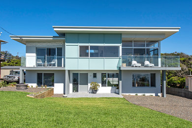 Photo of a mid-sized beach style two-storey blue house exterior in Other with mixed siding, a flat roof and a metal roof.