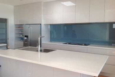 This is an example of a large contemporary galley eat-in kitchen in Wollongong with flat-panel cabinets, grey cabinets, quartz benchtops, blue splashback, glass sheet splashback, stainless steel appliances, medium hardwood floors and with island.