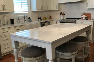 Example of a mid-sized farmhouse l-shaped eat-in kitchen design in Other with a farmhouse sink, beaded inset cabinets, white cabinets, quartz countertops, white backsplash, subway tile backsplash, stainless steel appliances, an island and white countertops