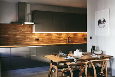 This is an example of a modern open plan kitchen in London with a drop-in sink, flat-panel cabinets, grey cabinets, wood benchtops, timber splashback, ceramic floors and grey floor.