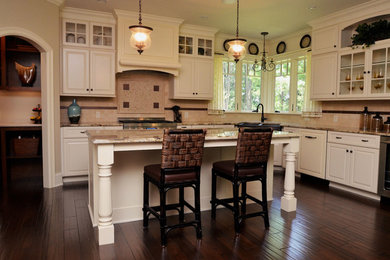 Elegant l-shaped dark wood floor and brown floor eat-in kitchen photo in New York with granite countertops, beige backsplash, stainless steel appliances, an island, an undermount sink, raised-panel cabinets, yellow cabinets and travertine backsplash