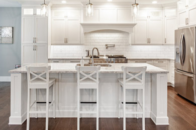 Open concept kitchen - mid-sized traditional l-shaped dark wood floor and brown floor open concept kitchen idea in Vancouver with an undermount sink, shaker cabinets, white cabinets, quartz countertops, white backsplash, ceramic backsplash, stainless steel appliances, an island and beige countertops