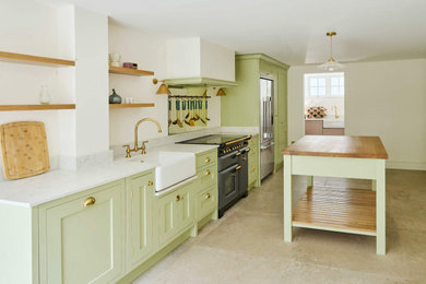 Inspiration for a single-wall kitchen/diner in London with a belfast sink, shaker cabinets, green cabinets, wood worktops, white splashback, black appliances, an island, brown worktops and feature lighting.