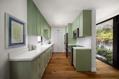 Example of a small arts and crafts galley medium tone wood floor and brown floor kitchen pantry design in Miami with a single-bowl sink, shaker cabinets, green cabinets, quartz countertops, white backsplash, quartz backsplash, stainless steel appliances, no island and white countertops