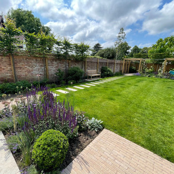 Full garden shot with pleached trees, pergolas and clay paver pathway.