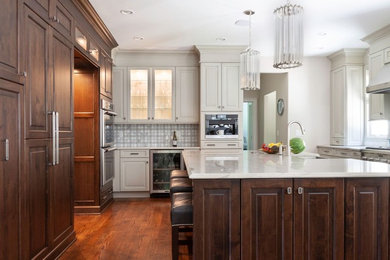 Large trendy l-shaped medium tone wood floor and brown floor eat-in kitchen photo in New York with a farmhouse sink, raised-panel cabinets, dark wood cabinets, marble countertops, gray backsplash, ceramic backsplash, stainless steel appliances, an island and white countertops