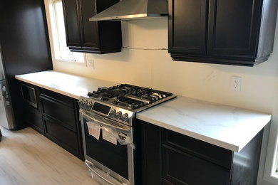 Mid-sized trendy single-wall laminate floor and gray floor eat-in kitchen photo in Toronto with an undermount sink, shaker cabinets, dark wood cabinets, quartz countertops, stainless steel appliances and an island
