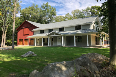 Foto della villa grande grigia country a due piani con rivestimento in legno, tetto a capanna, copertura a scandole, tetto grigio e pannelli sovrapposti