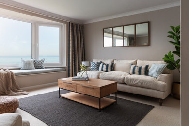 This is an example of a small beach style open plan living room in Cornwall with a reading nook, beige walls, carpet, no fireplace, a corner tv, beige floors and feature lighting.