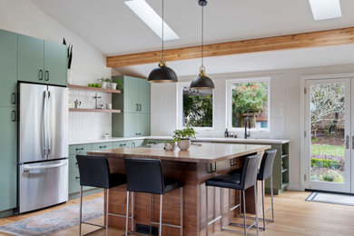 Example of a large l-shaped medium tone wood floor and vaulted ceiling open concept kitchen design in Seattle with an undermount sink, flat-panel cabinets, medium tone wood cabinets, wood countertops, white backsplash, ceramic backsplash, stainless steel appliances and an island