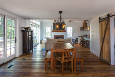 Mid-sized farmhouse medium tone wood floor, brown floor and exposed beam kitchen/dining room combo photo in Boston with white walls, a standard fireplace and a brick fireplace