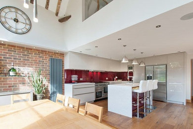 Design ideas for a contemporary kitchen in Sussex with a drop-in sink, flat-panel cabinets, red splashback, glass sheet splashback, stainless steel appliances, medium hardwood floors and with island.