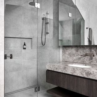 This is an example of a mid-sized contemporary master bathroom in Melbourne with furniture-like cabinets, dark wood cabinets, a freestanding tub, an alcove shower, a one-piece toilet, gray tile, ceramic tile, grey walls, ceramic floors, an undermount sink, limestone benchtops, grey floor, a hinged shower door, grey benchtops, a niche, a double vanity and a built-in vanity.