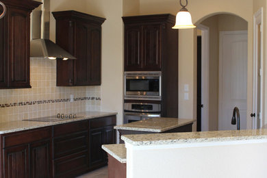 Kitchen photo in Austin with dark wood cabinets, beige backsplash, stainless steel appliances and an island