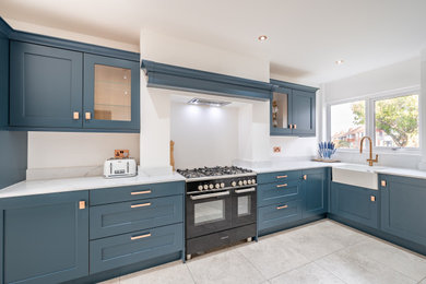 This is an example of a medium sized contemporary l-shaped kitchen/diner in Other with a belfast sink, shaker cabinets, blue cabinets, quartz worktops, integrated appliances, porcelain flooring, no island, white floors, white worktops, a vaulted ceiling and a chimney breast.