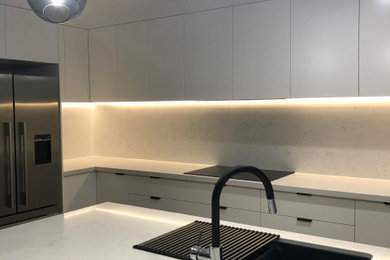 This is an example of a large contemporary l-shaped eat-in kitchen in Brisbane with an undermount sink, flat-panel cabinets, white cabinets, quartz benchtops, white splashback, stone slab splashback, black appliances, medium hardwood floors, with island, multi-coloured floor and white benchtop.