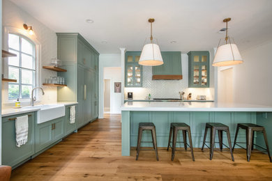 Huge transitional l-shaped medium tone wood floor and brown floor kitchen photo in Austin with a farmhouse sink, shaker cabinets, green cabinets, white backsplash, porcelain backsplash, paneled appliances, an island and white countertops