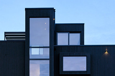 Diseño de fachada de casa negra actual de tres plantas con revestimiento de madera y tejado plano
