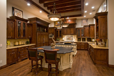 Example of a classic u-shaped dark wood floor kitchen design in Phoenix with a farmhouse sink, recessed-panel cabinets, dark wood cabinets, beige backsplash, ceramic backsplash, paneled appliances and two islands