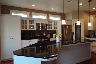 Inspiration for a large farmhouse galley medium tone wood floor eat-in kitchen remodel in Boise with a double-bowl sink, flat-panel cabinets, white cabinets, granite countertops, gray backsplash, subway tile backsplash and stainless steel appliances