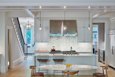 Example of a large transitional l-shaped light wood floor eat-in kitchen design in New York with a farmhouse sink, recessed-panel cabinets, white cabinets, quartz countertops, white backsplash, stainless steel appliances and an island