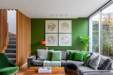 Photo of a large contemporary open concept living room in London with green walls, light hardwood floors and a wall-mounted tv.