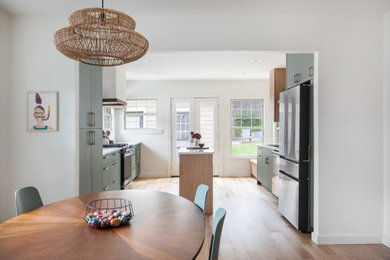 Open concept kitchen - mid-sized transitional galley light wood floor and brown floor open concept kitchen idea in Austin with an undermount sink, flat-panel cabinets, green cabinets, terrazzo countertops, white backsplash, porcelain backsplash, stainless steel appliances, an island and multicolored countertops