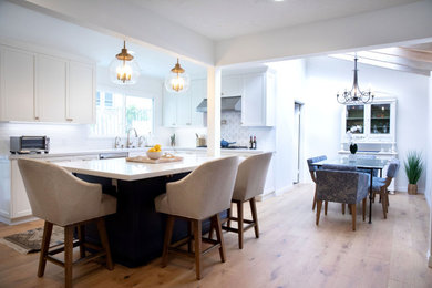 Kitchen - transitional light wood floor and beige floor kitchen idea in Los Angeles with a single-bowl sink, shaker cabinets, white cabinets, quartz countertops, white backsplash, ceramic backsplash, stainless steel appliances, an island and white countertops
