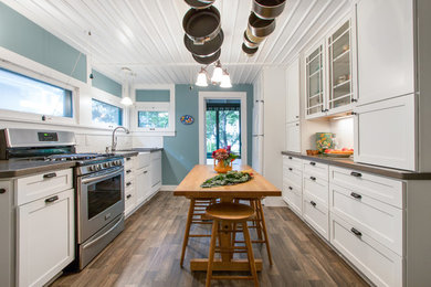 Small country galley separate kitchen in Milwaukee with a farmhouse sink, flat-panel cabinets, white cabinets, quartz benchtops, white splashback, ceramic splashback, stainless steel appliances, medium hardwood floors and no island.