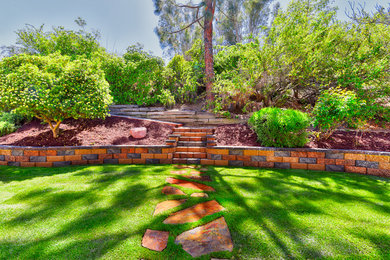 Design ideas for a mid-sized traditional sloped partial sun garden for spring in San Diego with a retaining wall and mulch.