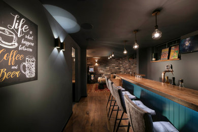 Imagen de sótano con ventanas industrial pequeño con bar en casa, paredes grises, suelo de madera en tonos medios y suelo marrón