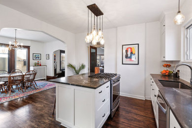 Mid-sized eclectic u-shaped dark wood floor and brown floor eat-in kitchen photo in Minneapolis with a single-bowl sink, flat-panel cabinets, white cabinets, quartz countertops, white backsplash, ceramic backsplash, stainless steel appliances, an island and black countertops