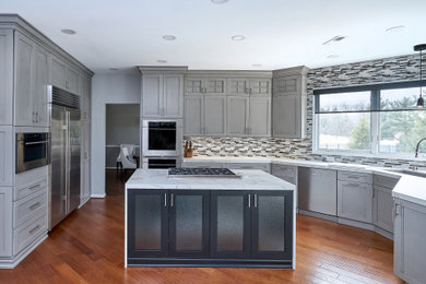 This is an example of a mid-sized transitional u-shaped eat-in kitchen in Philadelphia with flat-panel cabinets, grey cabinets, quartz benchtops, grey splashback, glass tile splashback, stainless steel appliances, with island and white benchtop.